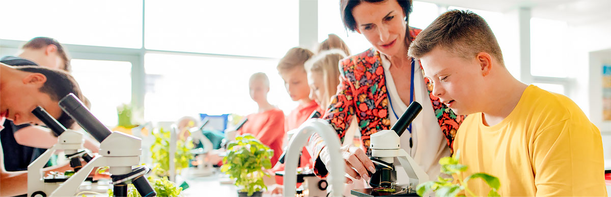 Student looking in microscope while teacher watches